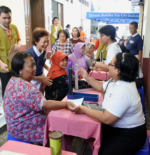 Karena lokasi baksos melewati lorong jalan yang sempit, para relawan Tzu Chi bersatu hati dan sigap membantu mengangkat kursi roda Vam Piin (80) menuju ke tempat pemeriksaan tekanan darah.